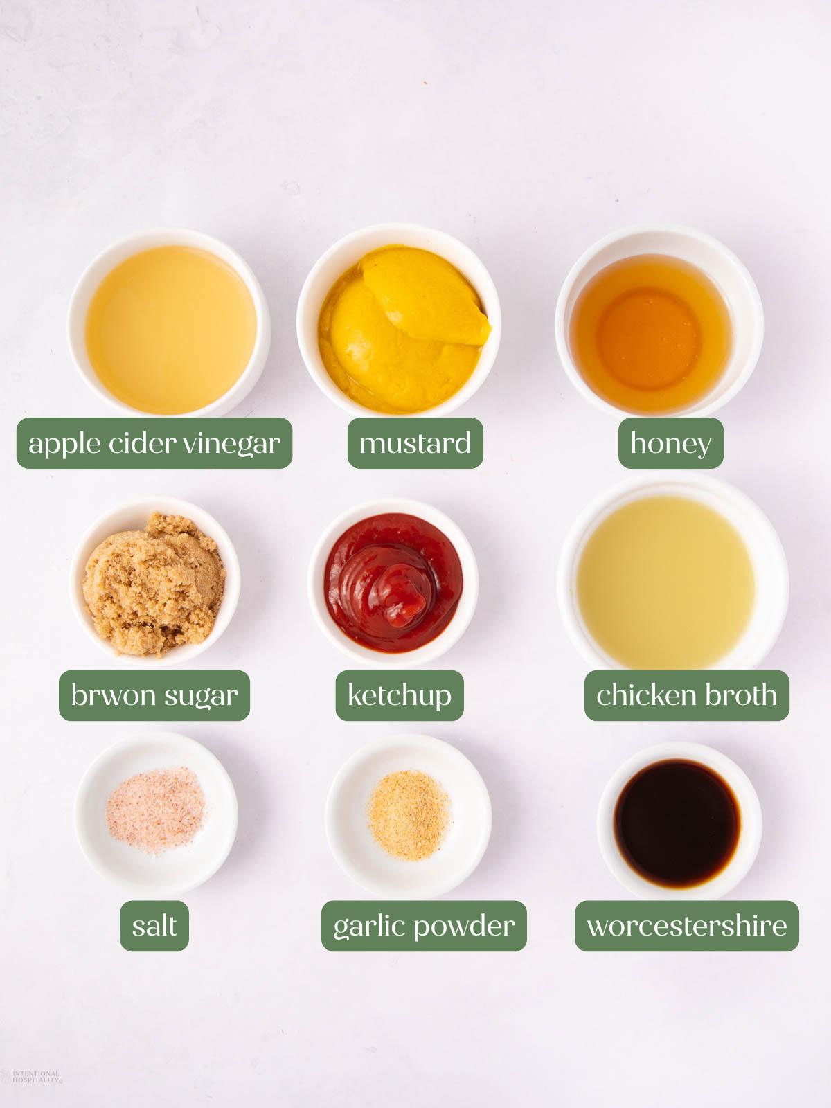 Nine small bowls with ingredients for a sauce are arranged on a white surface. They include apple cider vinegar, mustard, honey, brown sugar, ketchup, chicken broth, salt, garlic powder, and Worcestershire sauce.