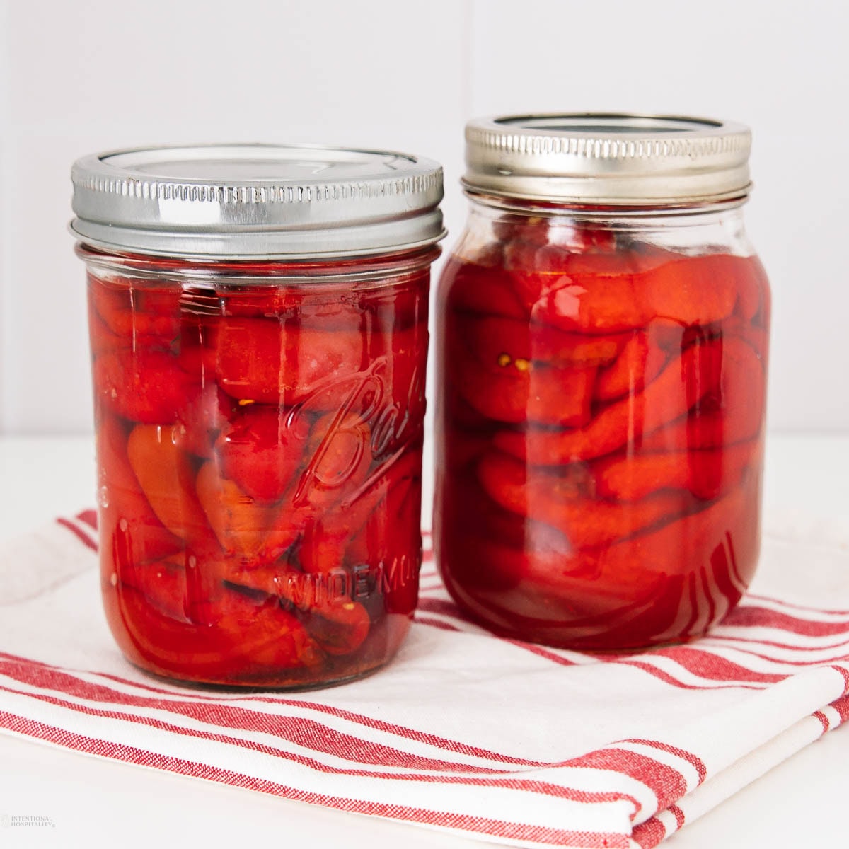 Two glass jars filled with red pickled peppers, sealed with metal lids