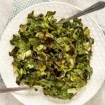 A plate of cooked collard greens mixed with chopped onions and a hint of canned cowboy candy recipe sweetness, served on a white hexagon-patterned plate with two silver forks.