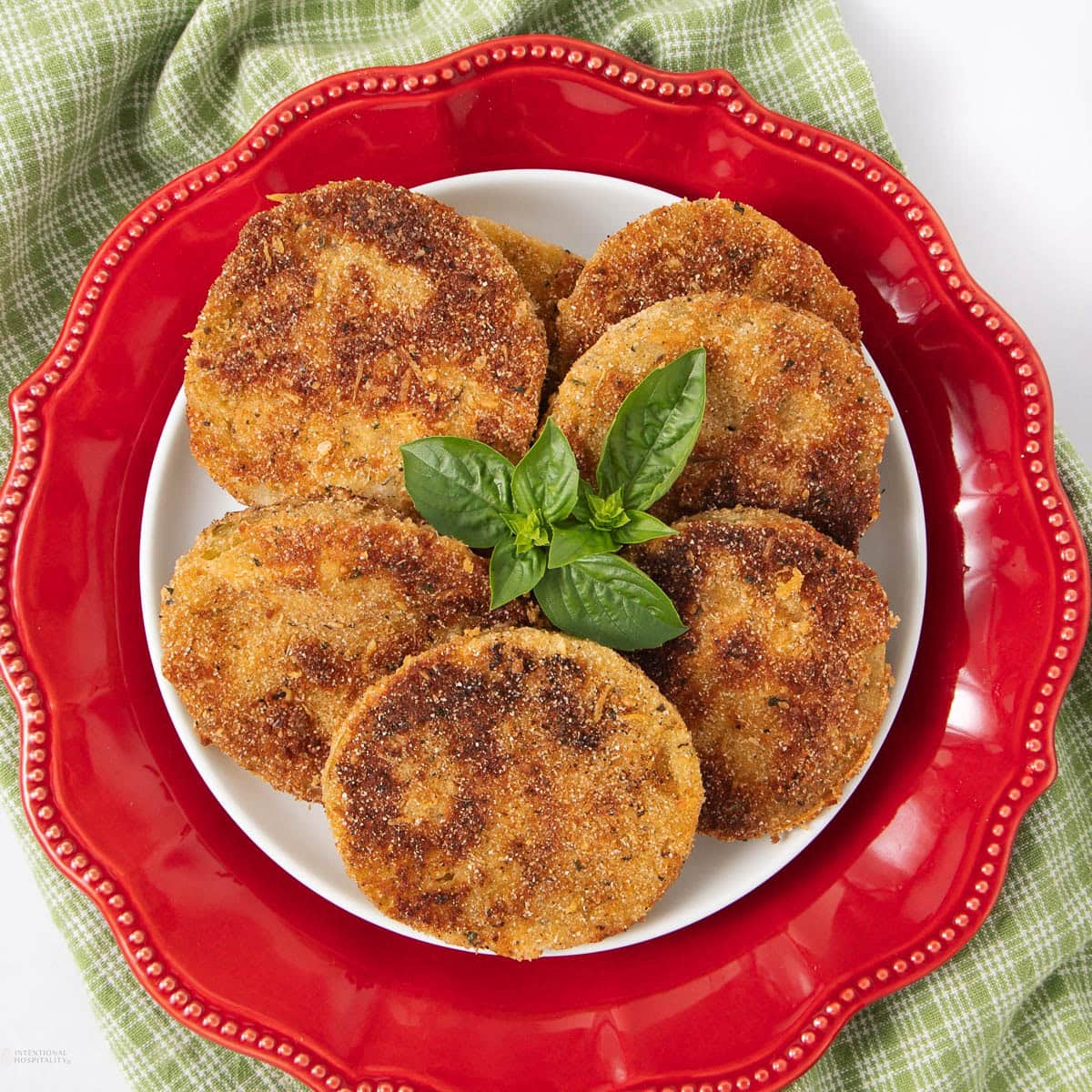 A plate of six golden-brown fried green tomato slices garnished with fresh basil.