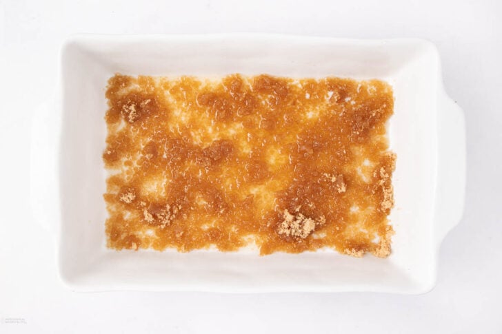 A white rectangular baking dish with an even layer of brown sugar spread across the bottom, photographed from above on a white background.