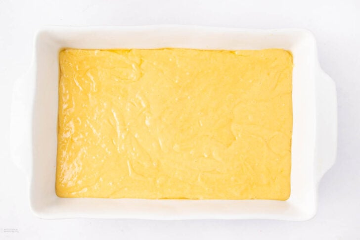 A white rectangular baking dish filled with an even layer of yellow cake batter, ready to be baked.