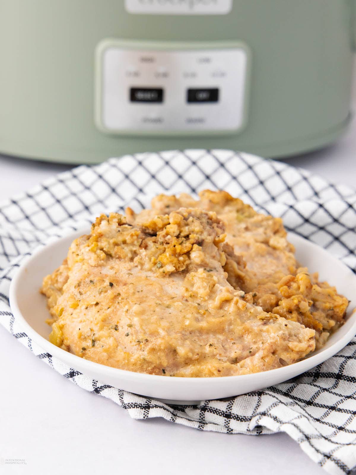 A serving of creamy chicken and stuffing on a white plate, placed on a black-and-white checkered cloth with a slow cooker in the background.