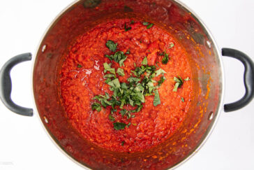 A pot filled with chunky red tomato sauce topped with freshly chopped green basil, viewed from above against a white background.