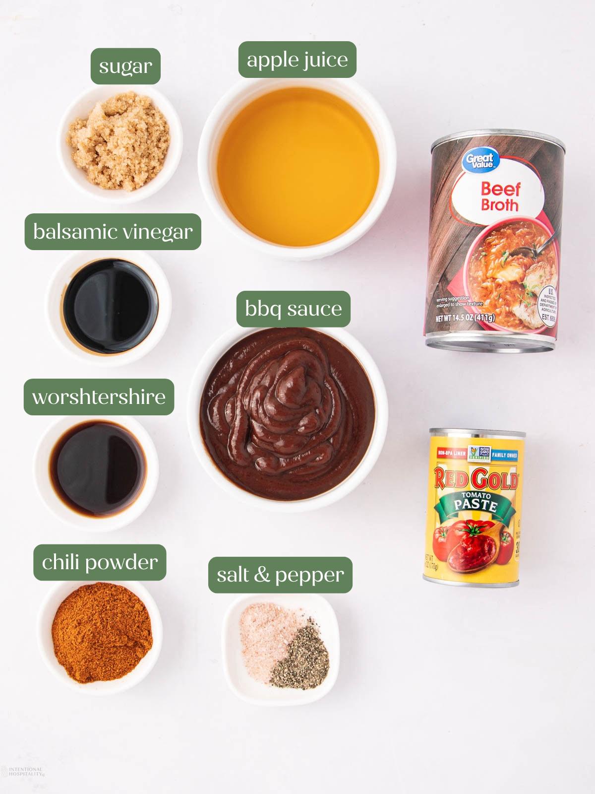 A top view of ingredients for a BBQ sauce: brown sugar, apple juice, beef broth, balsamic vinegar, Worcestershire sauce, BBQ sauce, tomato paste, chili powder, salt, and pepper in separate bowls and cans, all labeled.