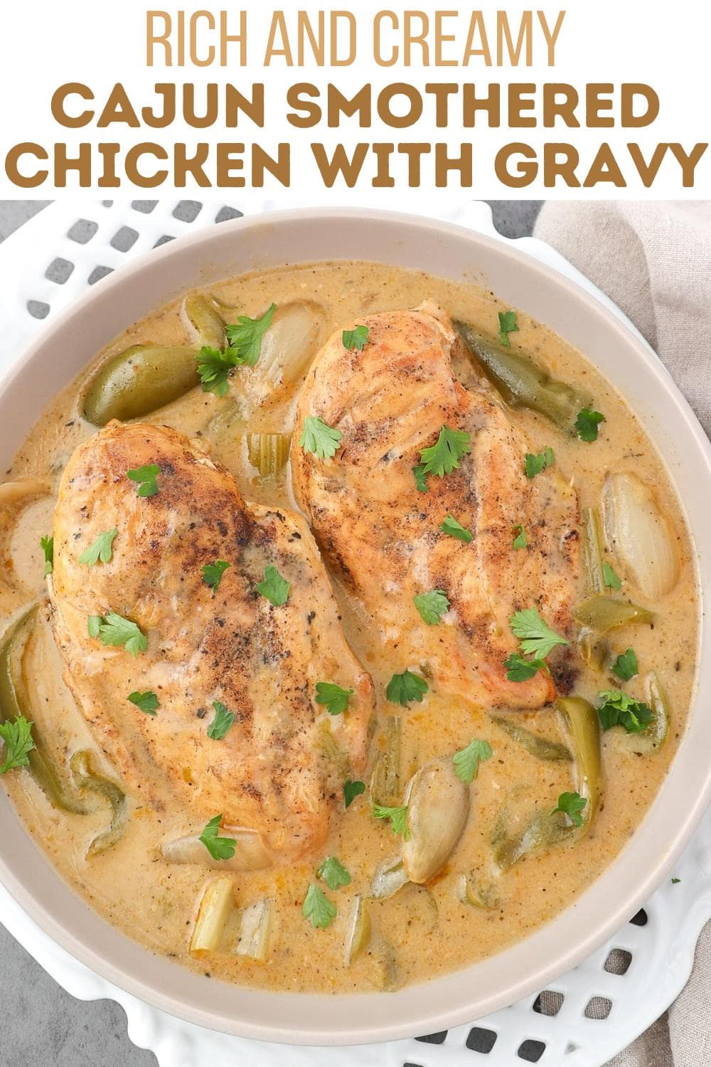 A bowl of rich, creamy Cajun chicken with gravy, featuring two seasoned chicken breasts, green bell peppers, onions, and fresh parsley, garnished on top. Text above reads "Rich and Creamy Cajun Smothered Chicken with Gravy.
