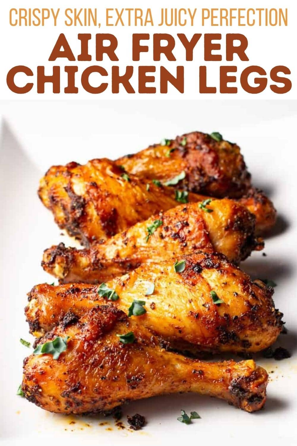 Four golden-brown, seasoned chicken drumsticks garnished with fresh herbs on a white plate. Text above reads: "Crispy skin, extra juicy perfection. Air fryer chicken legs.