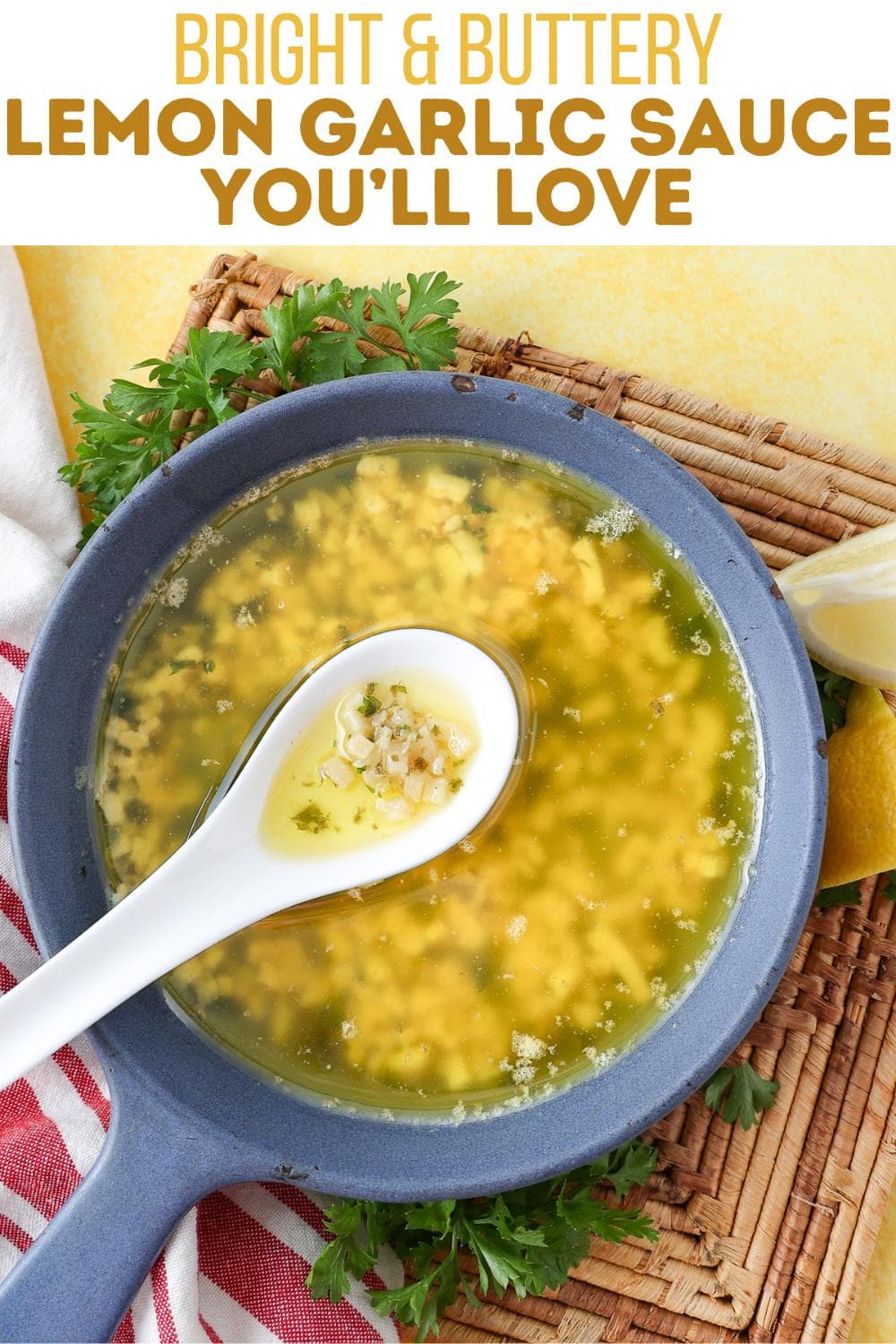 A blue pan filled with a bright yellow lemon garlic sauce sits on a woven mat, garnished with parsley. A white ceramic spoon with sauce rests on the pan. Text above reads: "Bright & Buttery Lemon Garlic Sauce You'll Love.
