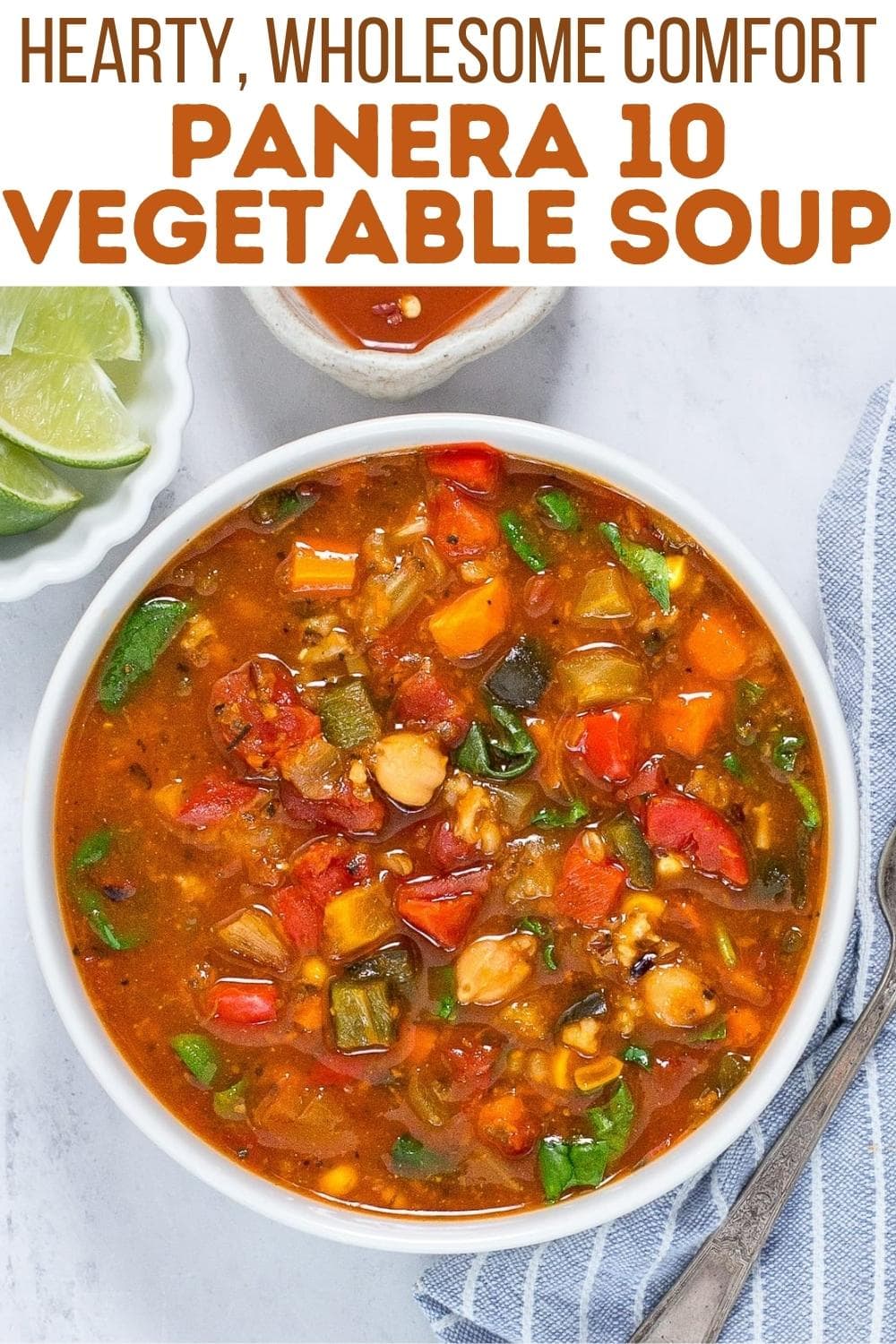 A bowl of colorful vegetable soup with tomatoes, beans, and greens sits on a white table next to lime wedges and a striped napkin, under text reading "Hearty, Wholesome Comfort Panera 10 Vegetable Soup.