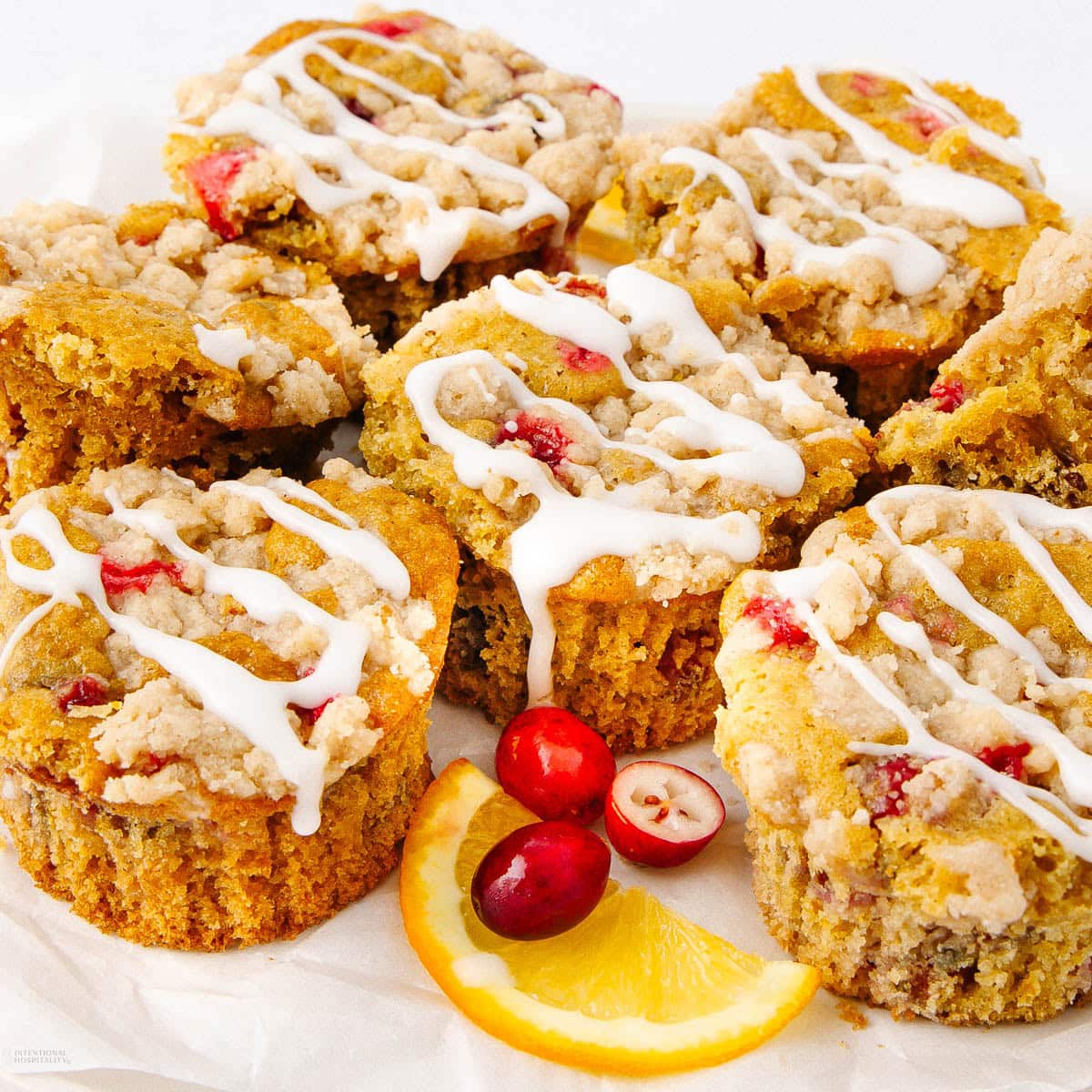 Seven cranberry-orange muffins with crumb topping and white icing drizzle