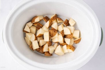 Diced potatoes with skin on are placed inside a white slow cooker, ready to be cooked.