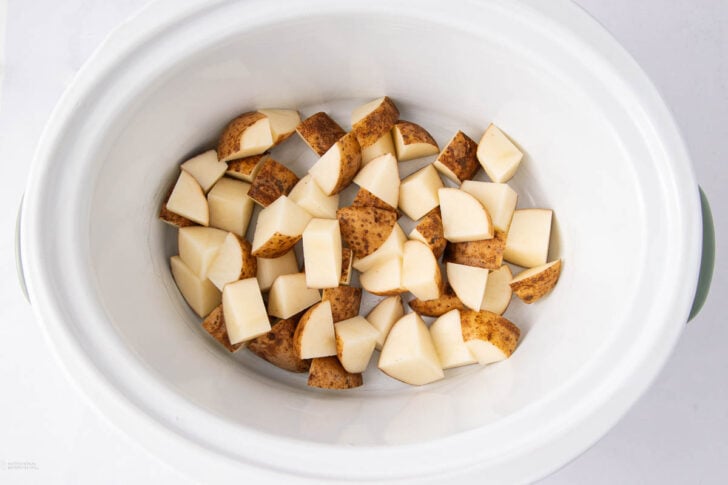Diced potatoes with skin on are placed inside a white slow cooker, ready to be cooked.