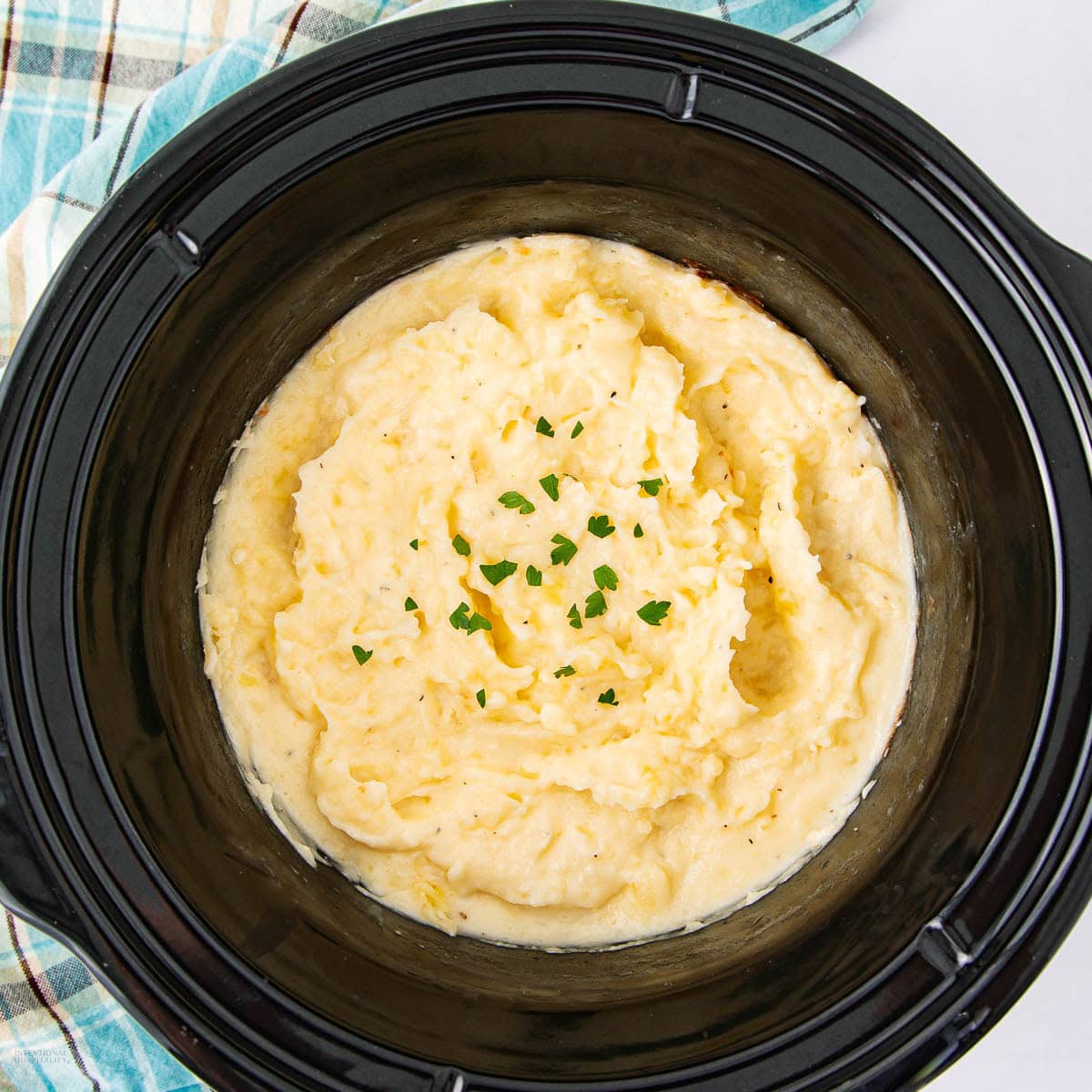 Creamy mashed potatoes garnished with chopped parsley in a black slow cooker