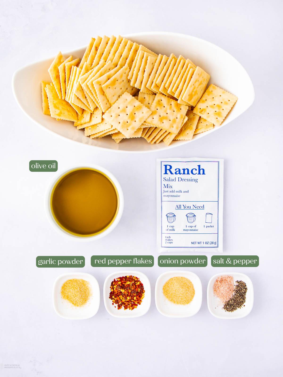 Oval dish of saltine crackers, a bowl of olive oil, a packet of ranch salad dressing mix, and small dishes with garlic powder, red pepper flakes, onion powder, and a mix of salt and pepper, all labeled.