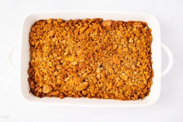 A white rectangular baking dish filled with a golden brown, crumbly baked topping, likely a crisp or crumble dessert, on a plain white background.