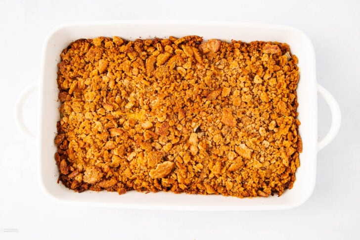 A white rectangular baking dish filled with a golden brown, crumbly baked topping, likely a crisp or crumble dessert, on a plain white background.