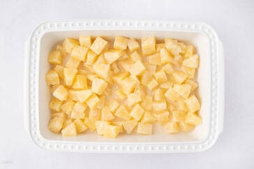 A white rectangular dish filled with evenly spread chunks of pineapple on a light background.
