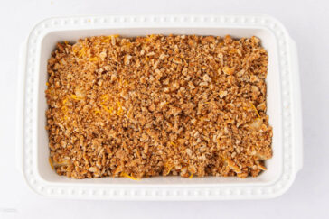 A white rectangular baking dish filled with a golden brown crumbly casserole topping, possibly made of breadcrumbs or crushed crackers, on a plain white background.