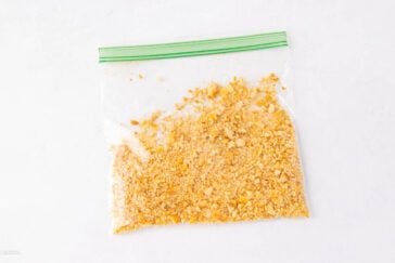 A clear plastic zip-top bag filled with finely crushed yellow cracker crumbs sits on a white surface.