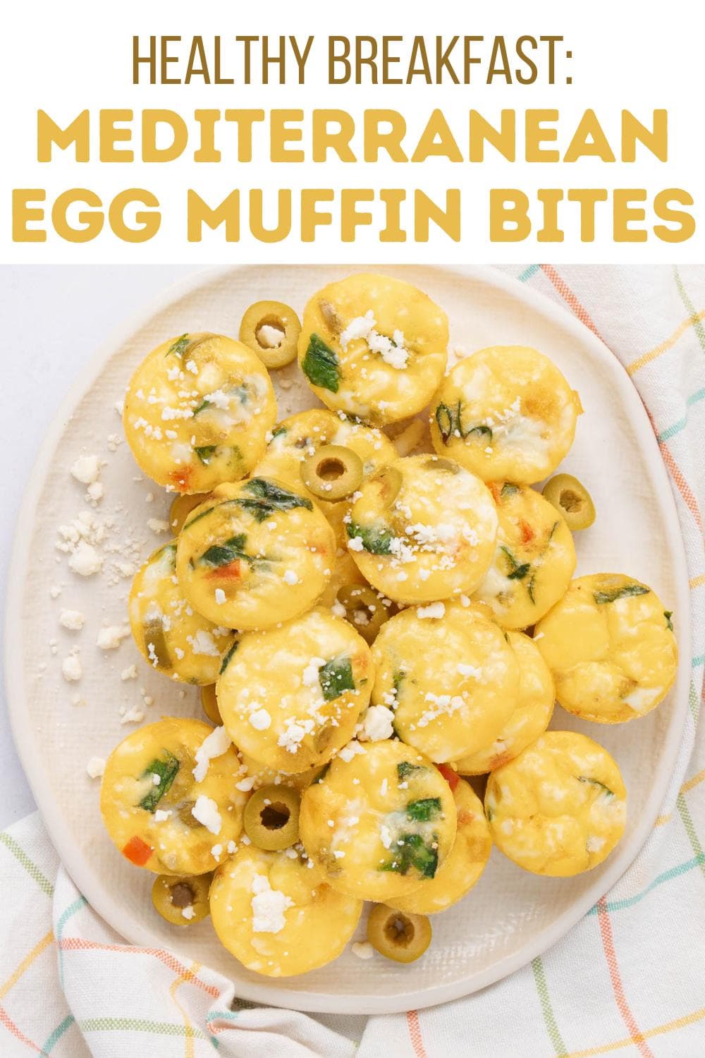 A plate of Mediterranean egg muffin bites topped with crumbled feta and vegetables, arranged on a white platter with a light checkered cloth beside it. Text above reads “Healthy Breakfast: Mediterranean Egg Muffin Bites.”.