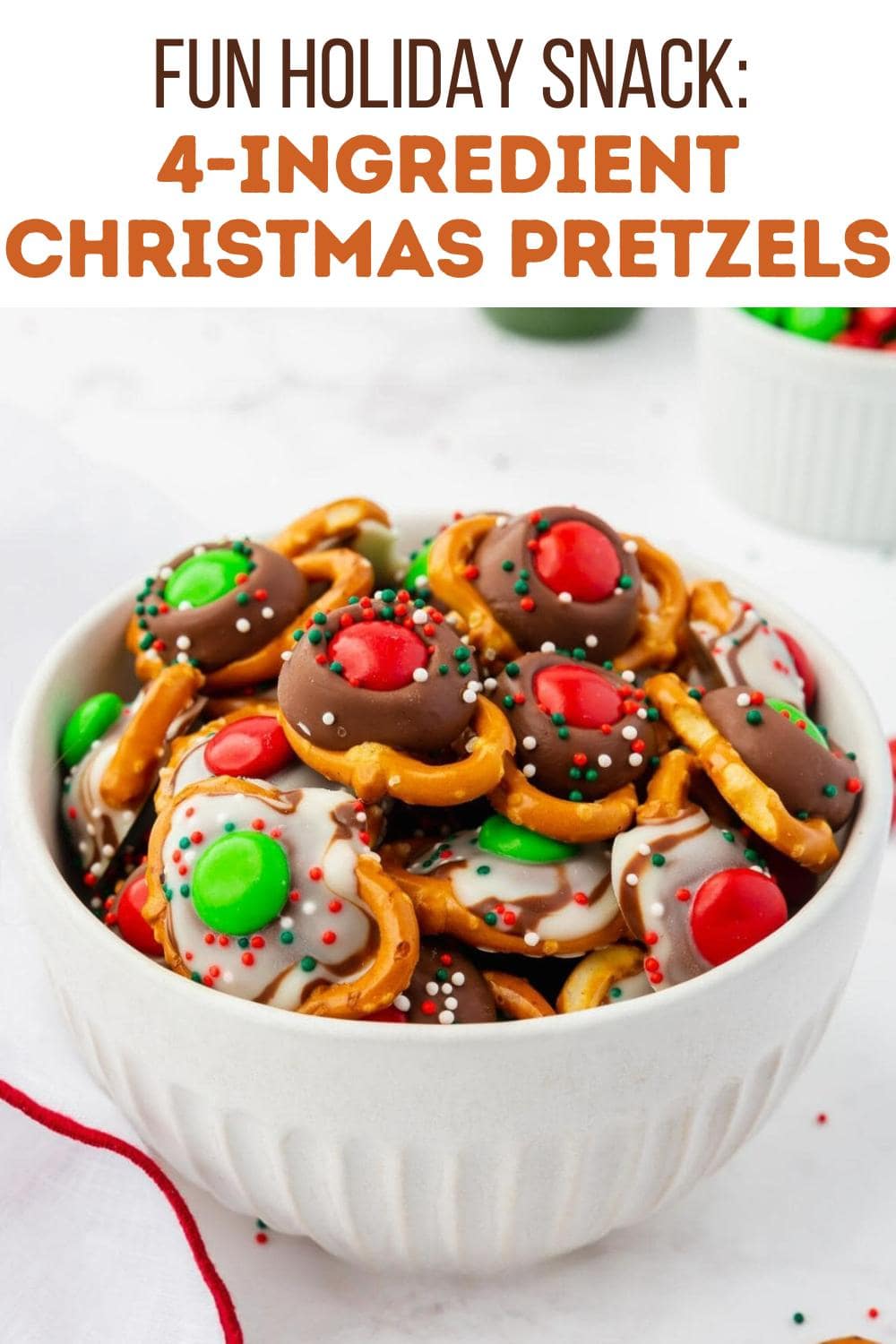 A white bowl filled with holiday pretzels topped with chocolate, red and green candies, and festive sprinkles. Text above reads: "Fun Holiday Snack: 4-Ingredient Christmas Pretzels.