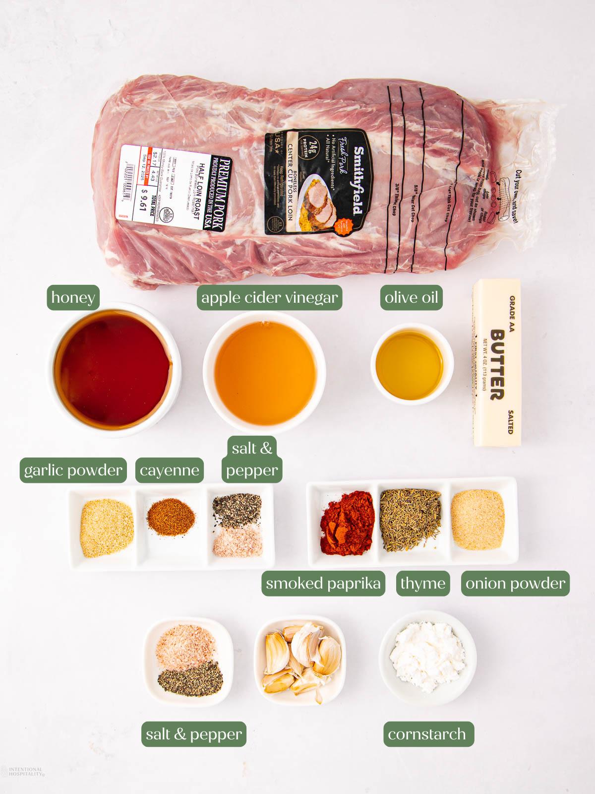 Raw pork shoulder roast with labeled ingredients around it: honey, apple cider vinegar, olive oil, butter, garlic powder, cayenne, salt & pepper, thyme, smoked paprika, onion powder, whole garlic, and cornstarch.