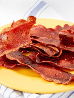Crispy slices of vegan bacon arranged on a yellow plate, placed on a white cloth with blue stripes.