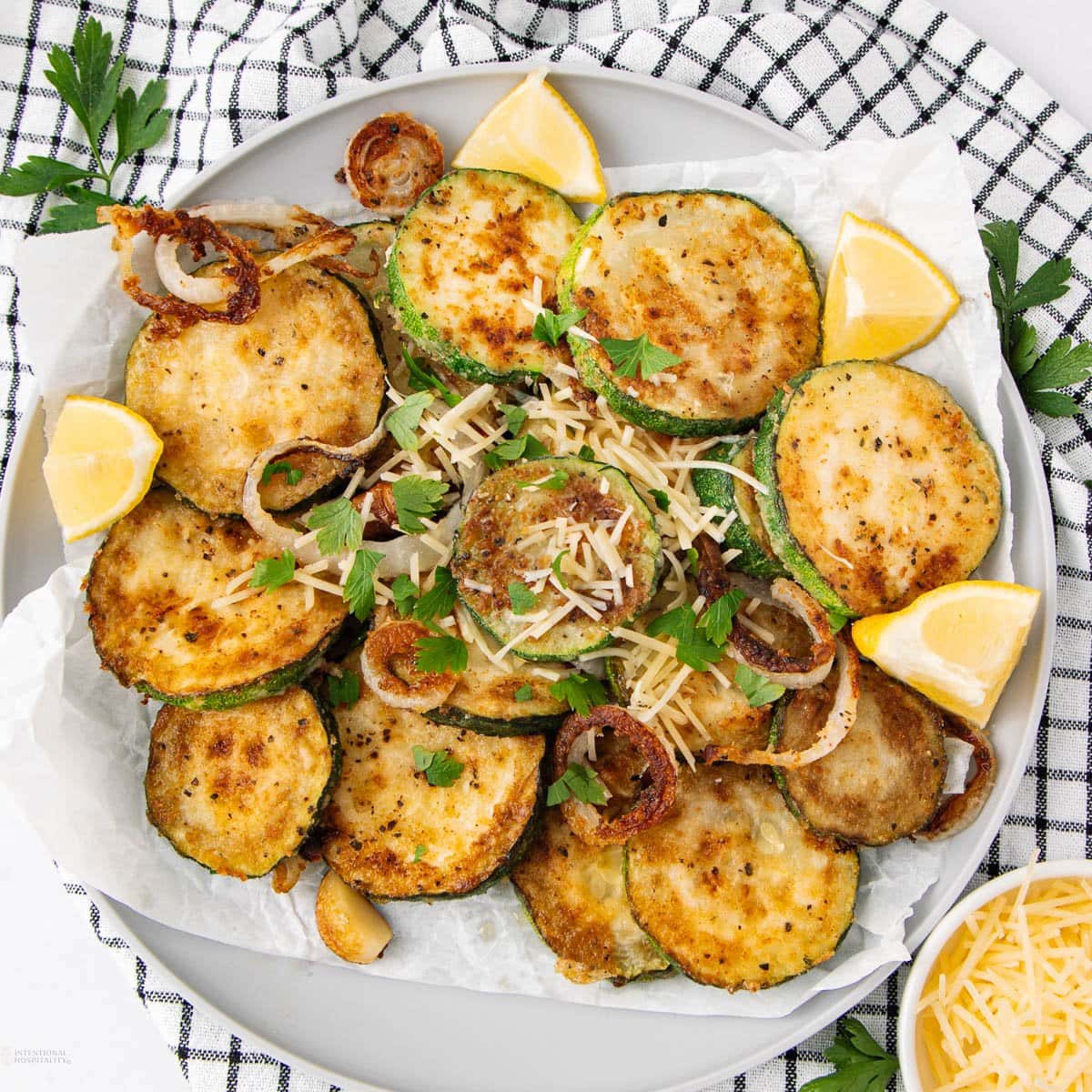 A plate of golden-brown, breaded fried zucchini slices garnished with parsley, grated chees