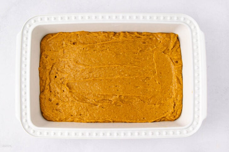 A white rectangular baking dish filled with an even layer of uncooked pumpkin batter, ready to be baked.