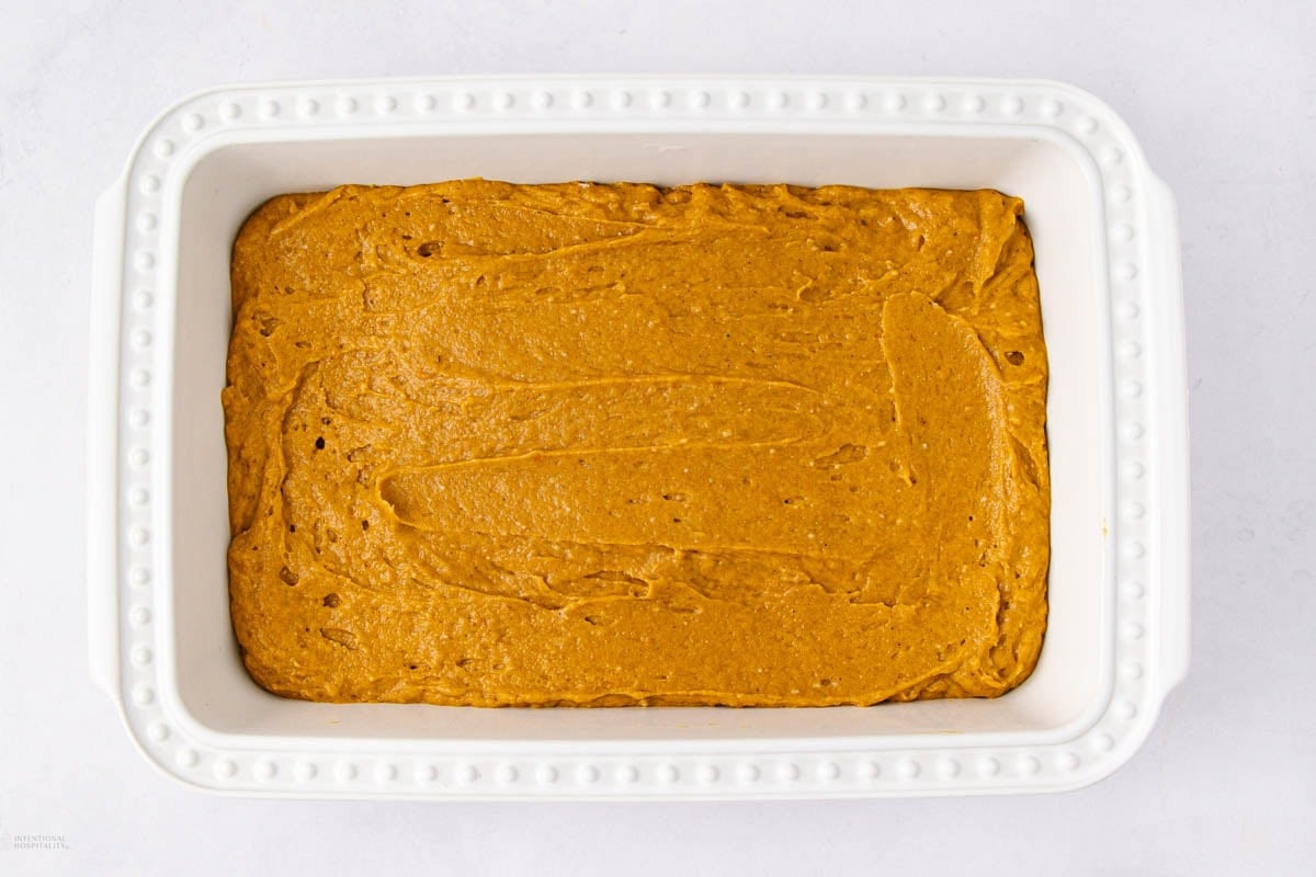 A white rectangular baking dish filled with an even layer of uncooked pumpkin batter, ready to be baked.