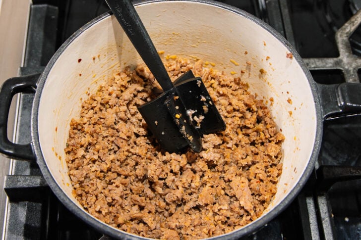 Cooked ground meat seasoned with spices fills a large pot on a stovetop, with a black spatula resting inside for stirring.