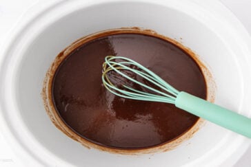 A light green whisk mixing smooth, glossy chocolate batter in a white mixing bowl.