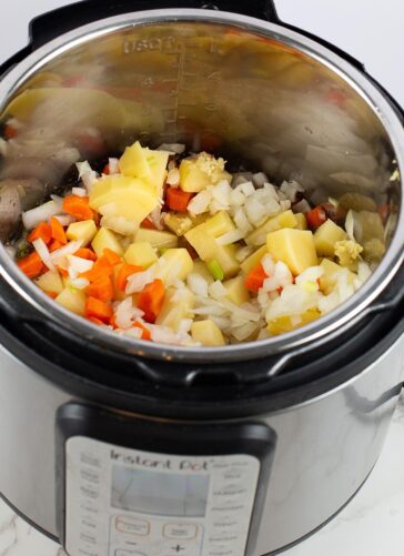 Chopped potatoes, carrots, onions, and garlic are inside an Instant Pot, ready to be cooked. The ingredients are uncooked and the pot is open on a white surface.