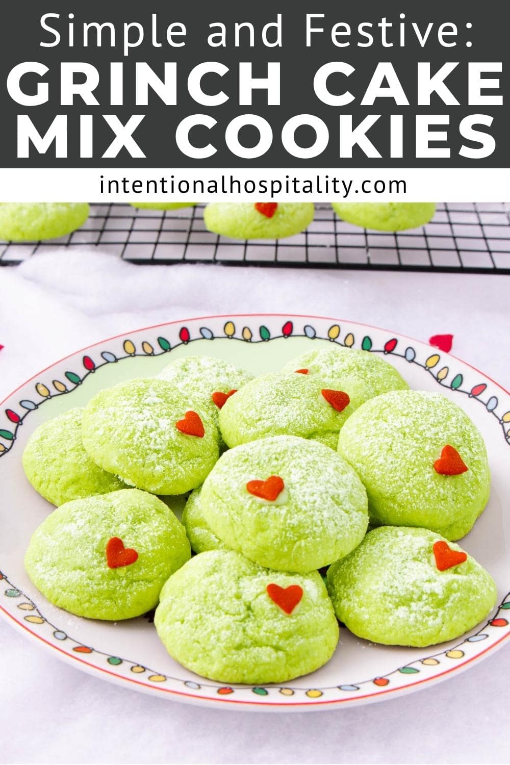 A colorful plate holds bright green cookies dusted with powdered sugar, each topped with a small red heart. More cookies cool on a wire rack in the background. Text above reads, "Simple and Festive: Grinch Cake Mix Cookies.