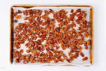 A baking sheet lined with parchment paper is covered with a single layer of roasted pecans.