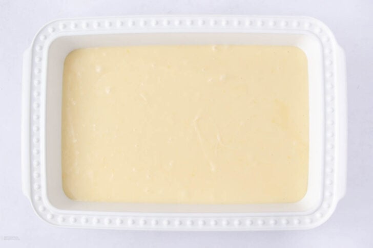 A white rectangular baking dish filled with smooth, pale yellow cheesecake batter, ready to be baked.
