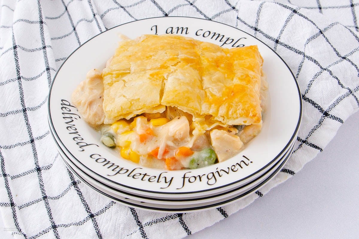 A slice of golden-brown pot pie with vegetables and chicken on a plate with the words “I am completely delivered, completely forgiven!” set on a white checked cloth.