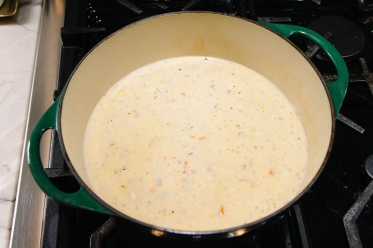 A large green Dutch oven sits on a stove, filled with a creamy, light-colored soup containing small bits of vegetables.