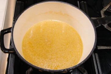 A Dutch oven filled with simmering chicken broth sits on a stovetop, with a layer of yellow fat visible on the surface of the liquid.
