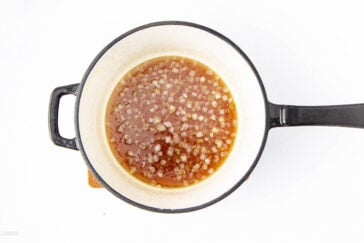 A white pot with a black handle containing a mixture of diced onions and broth or sauce, viewed from above on a white background.