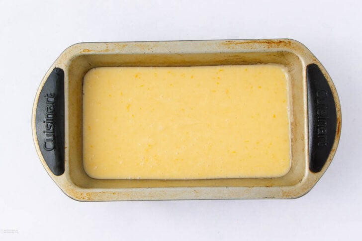 A metal loaf pan filled with an unbaked yellow batter, viewed from above, on a white background.