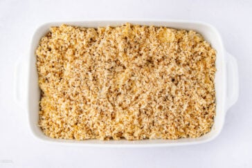 A white rectangular baking dish filled with macaroni and cheese, topped with a golden, crumbly breadcrumb layer, ready to be baked.