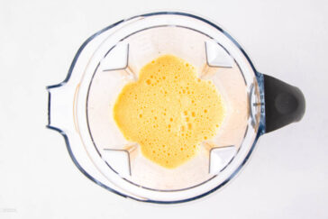 A top-down view of a blender containing a frothy, yellow liquid mixture against a white background.