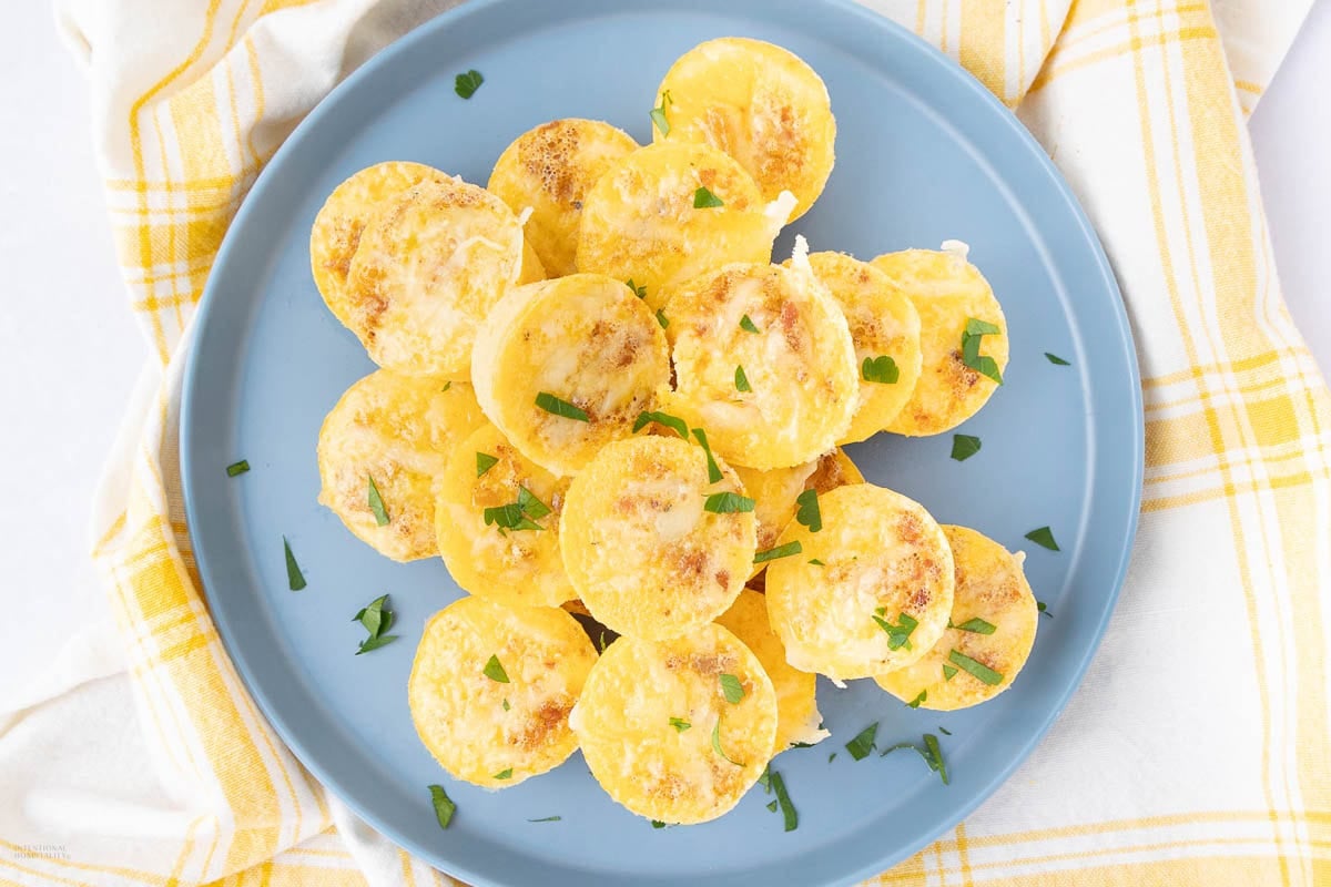 A blue plate filled with small, round, baked egg bites garnished with chopped herbs, placed on a yellow and white checkered cloth.
