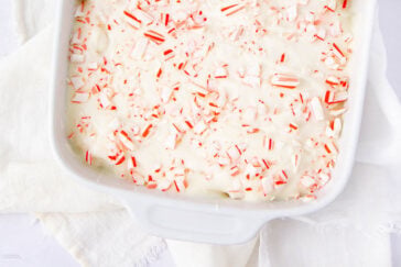 A white baking dish filled with white chocolate bark topped with crushed peppermint candy pieces, sitting on a white cloth.