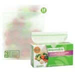 A green and white box labeled "Responsible Resealable Zip Food Bags" sits next to a semi-transparent compostable zip bag containing produce. The box states it contains 58 quart-size compostable bags.