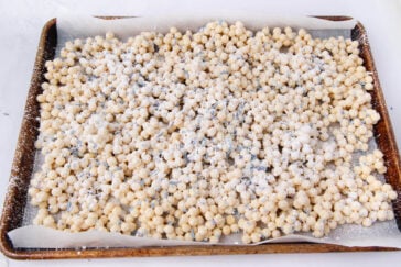 A baking sheet lined with parchment paper is covered in small, round balls of dough coated with flour, spread out in a single layer.