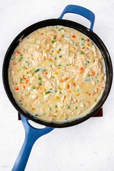 A blue skillet filled with creamy chicken pot pie filling, featuring shredded chicken, peas, carrots, corn, and green beans in a thick white sauce.