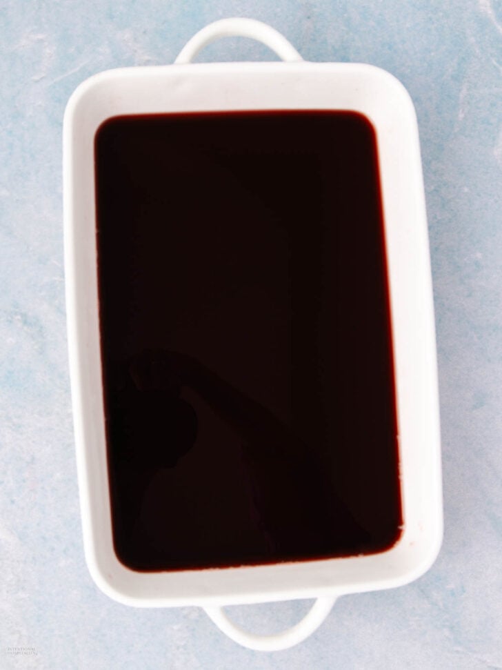 A rectangular white dish filled with a dark red liquid, placed on a light blue surface.