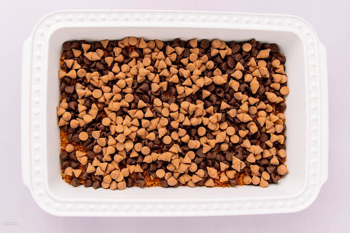 A white rectangular baking dish filled with a layer of peanut butter and chocolate chips, evenly spread across the top.
